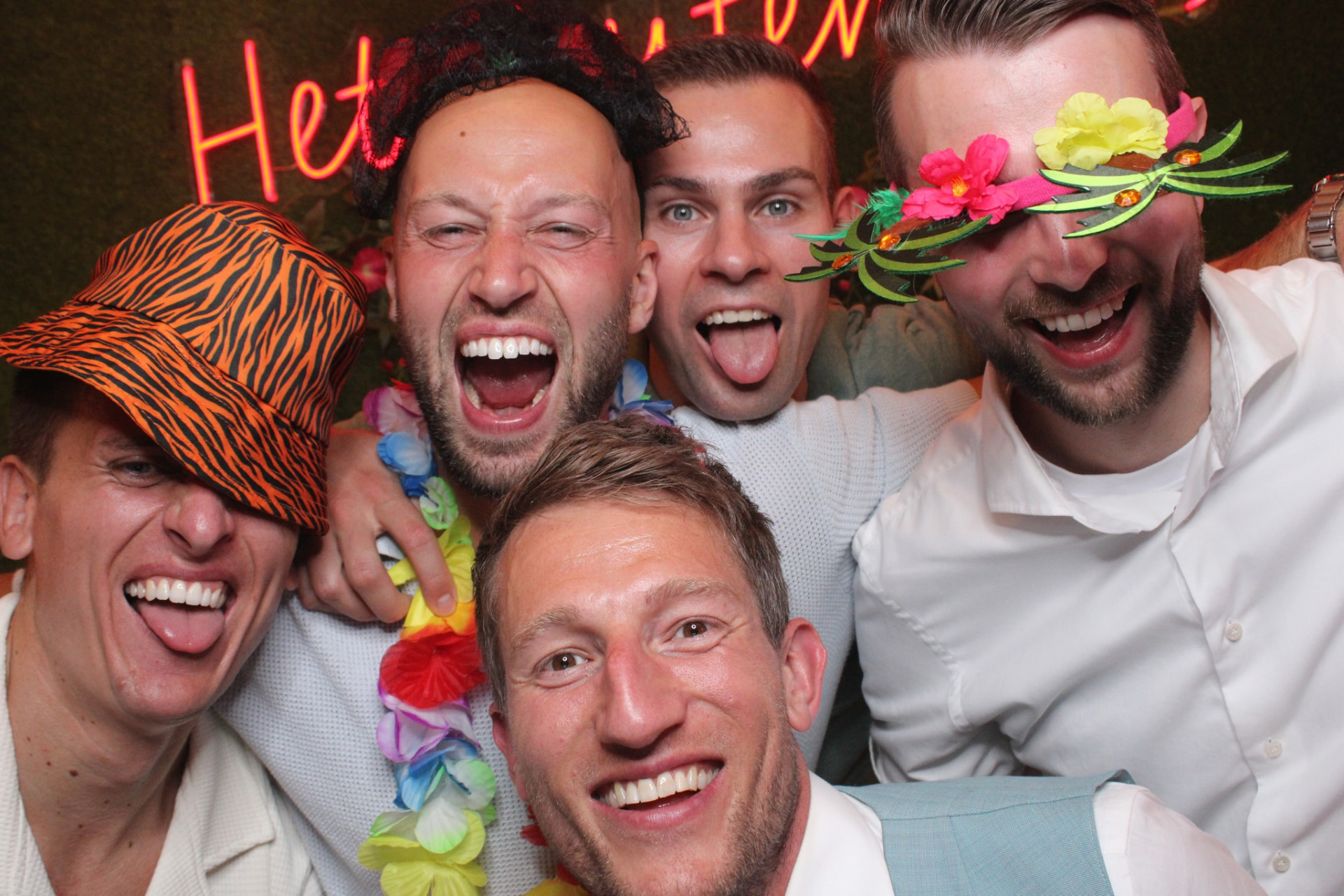 Vrolijke groep met photoboothprops voor de neonwand – verhuur door Uitjes2go in Ede