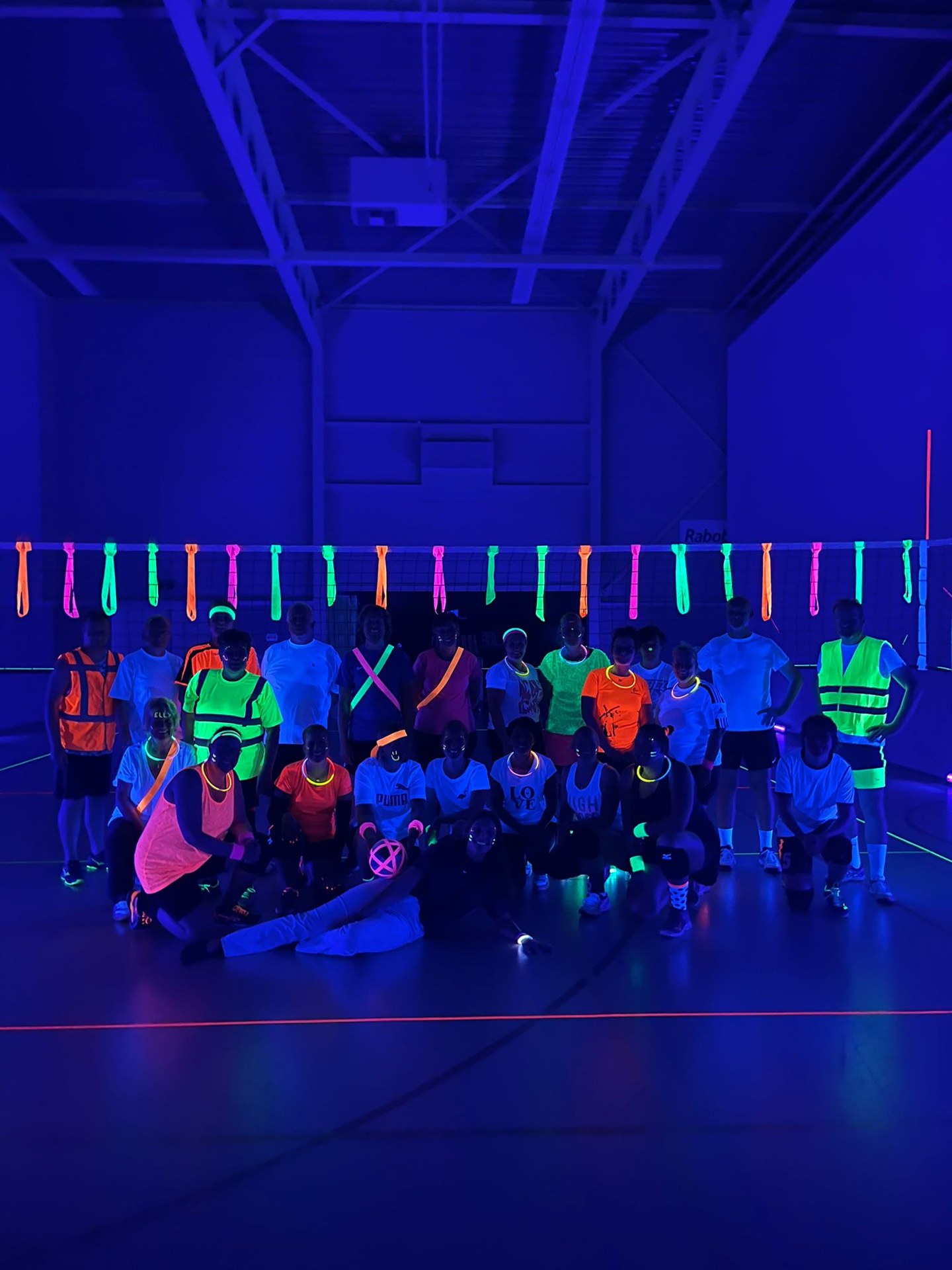 Groep in een sporthal onder blacklight met neonmaterialen – verhuur door Uitjes2go in Ede